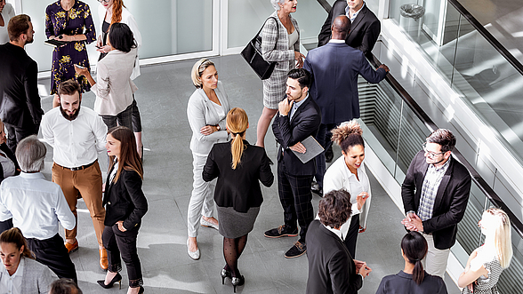 © sanjeri – istock.com Menschen stehen in Gruppen zusammen und unterhalten sich.