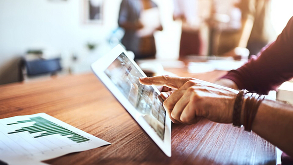 © PeopleImages – istock.com  Person hat Tablet in der Hand und sieht sich eine Webseite an