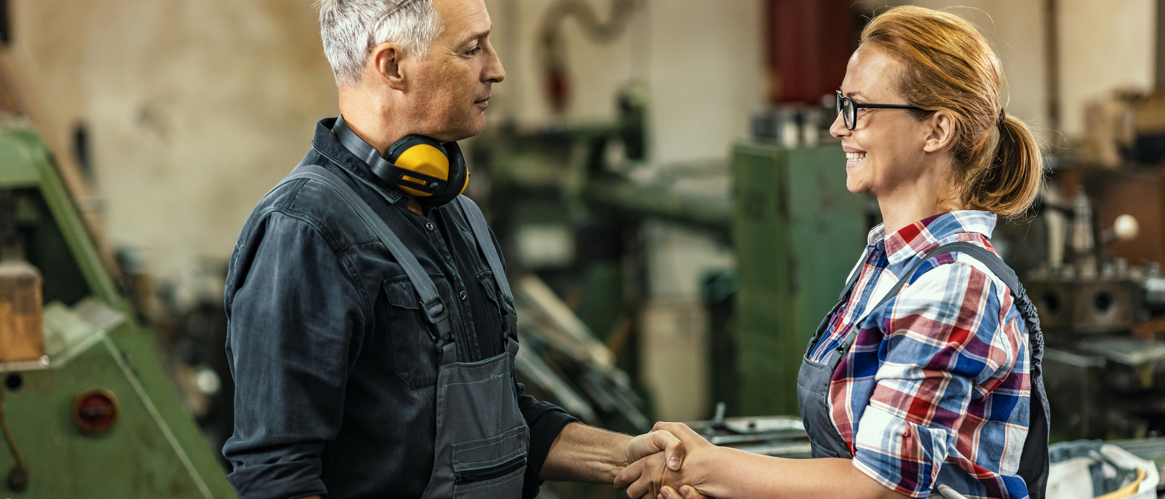 © ljubaphoto - iStock.com Ein Mann schüttelt einer Frau in einer Werkstatt die Hand.