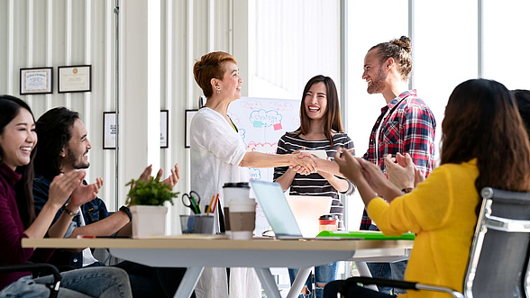 © Chaay_Tee– istock.com Bürosituation, Frau heißt neuen Mitarbeiter willkommen