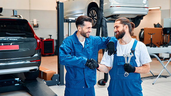 © Valerii Apetroaiei - iStock Zwei Herren schütteln sich in einer Autowerkstatt die Hände und lächeln sich an.