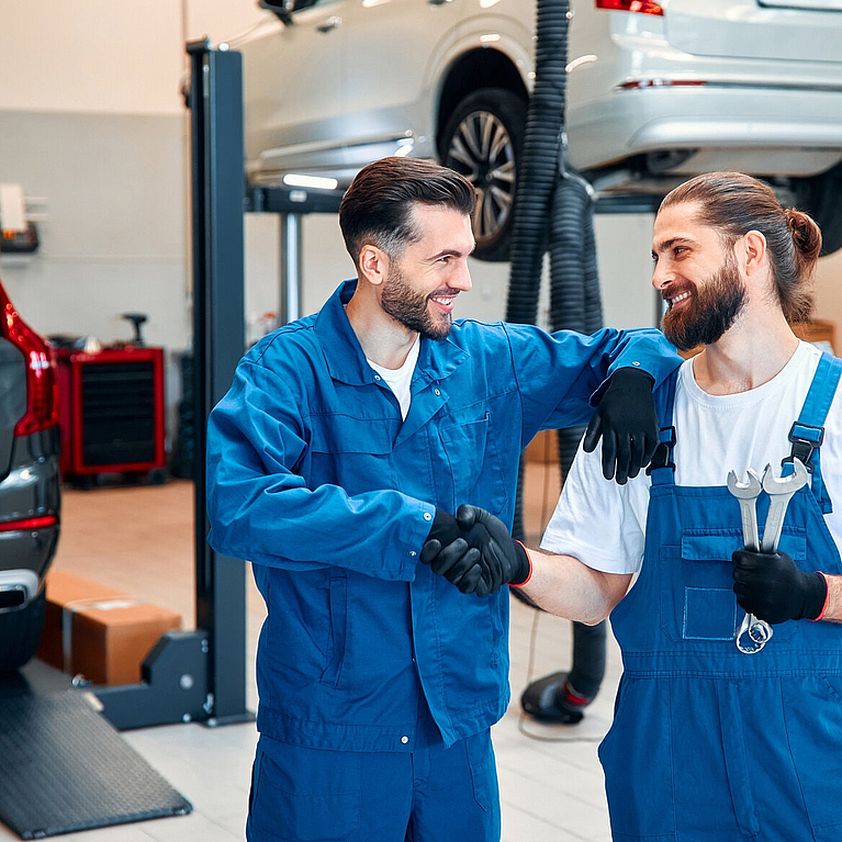 Zwei Herren schütteln sich in einer Autowerkstatt die Hände und lächeln sich an.