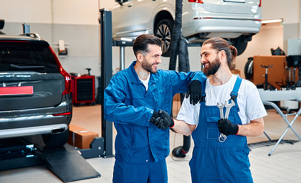 Zwei Herren schütteln sich in einer Autowerkstatt die Hände und lächeln sich an.